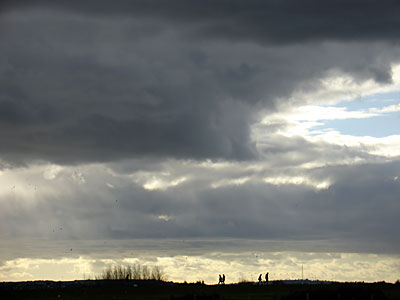 Dramatic winter sky and walkers, walking to Camber sands, Rye, Sussex, UK