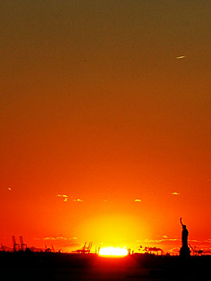 Dying light of the sun against the Statue of Liberty, Brooklyn Bridge, New York, USA