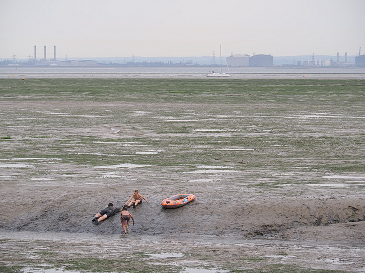 Swimmers and stranded boats on a sea of mud in the shadow of the oil refineries: Leigh on Sea in the summer 