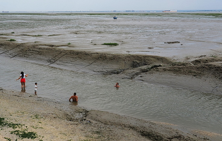 Swimmers and stranded boats on a sea of mud in the shadow of the oil refineries: Leigh on Sea in the summer 