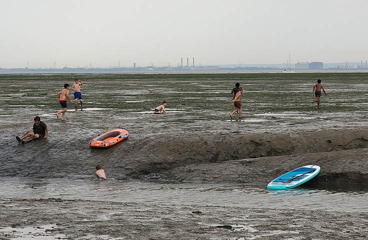 Swimmers and stranded boats on a sea of mud in the shadow of the oil refineries: Leigh on Sea in the summer 
