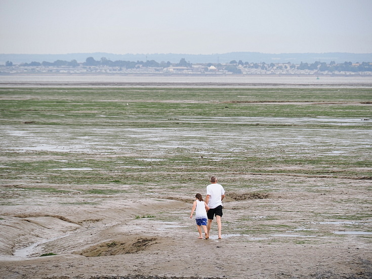 Swimmers and stranded boats on a sea of mud in the shadow of the oil refineries: Leigh on Sea in the summer 