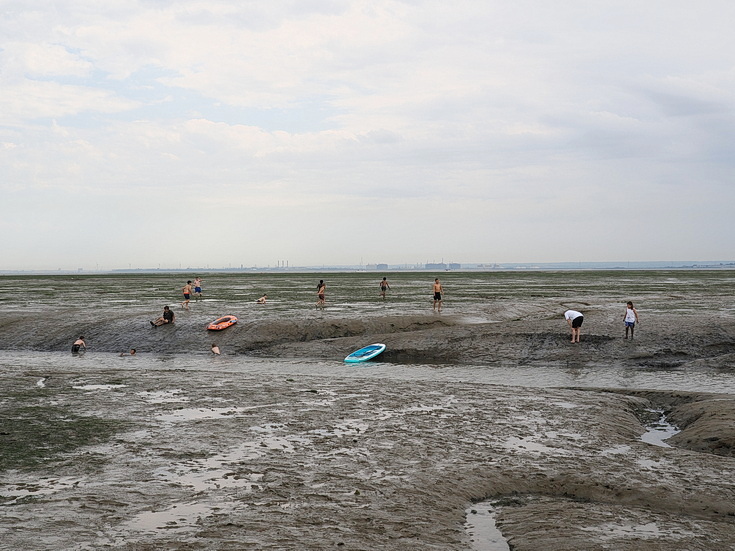 Swimmers and stranded boats on a sea of mud in the shadow of the oil refineries: Leigh on Sea in the summer 
