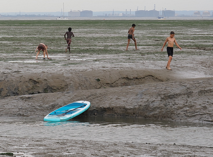 Swimmers and stranded boats on a sea of mud in the shadow of the oil refineries: Leigh on Sea in the summer 